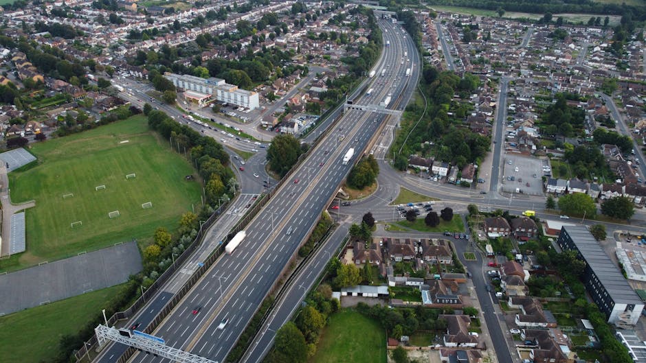 Aerial view of the Willesden Junction to Brent Park area showing a multi-lane motorway with several trucks and cars traveling along the road. The motorway passes over a small junction with intersectin